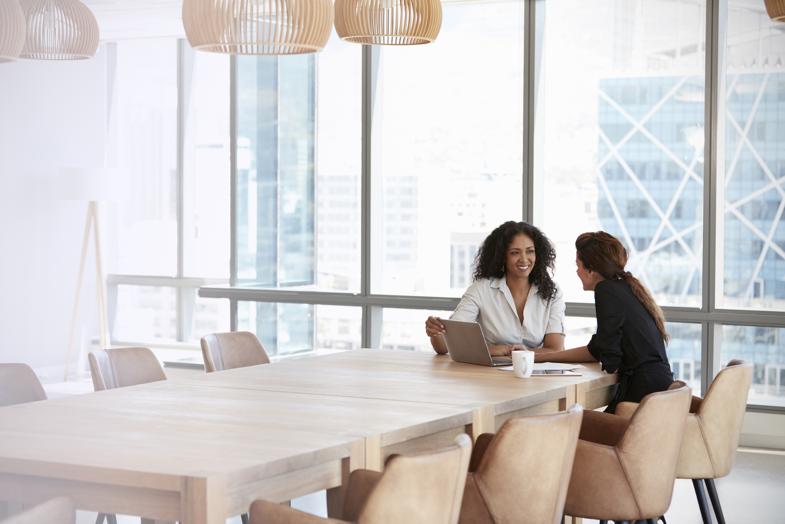 Two women having a meeting in a modern office with large windows.