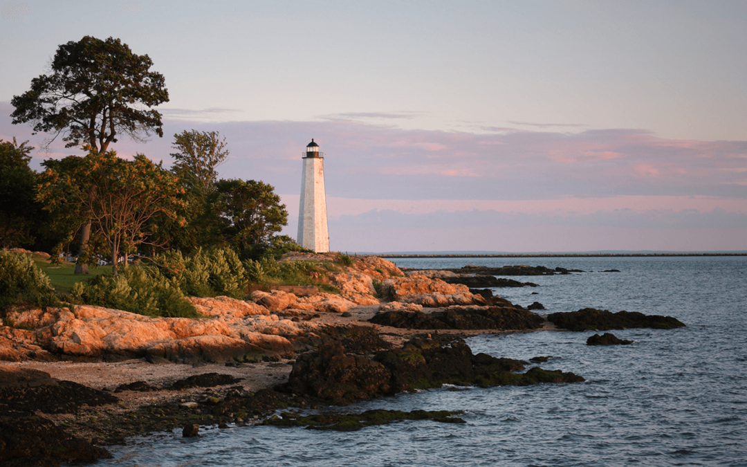 Coastal lighthouse at sunset with rocky shore and trees