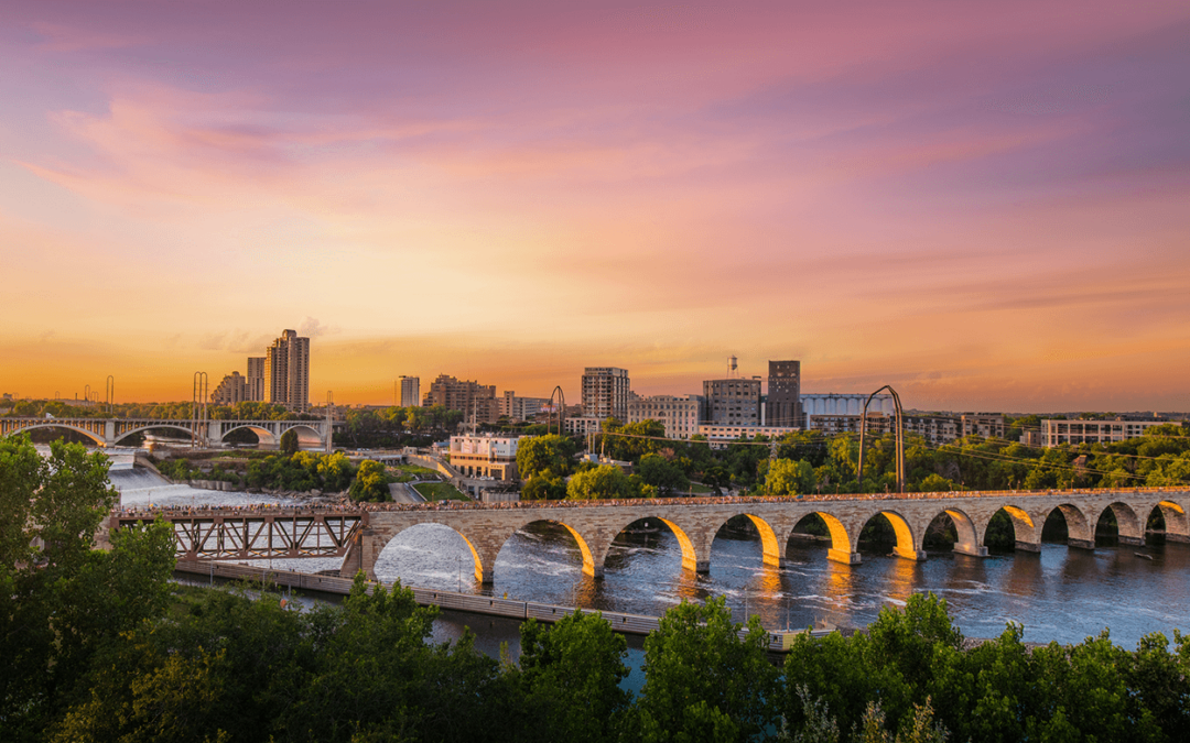 A vibrant sunset over a historic stone arch bridge and city skyline.