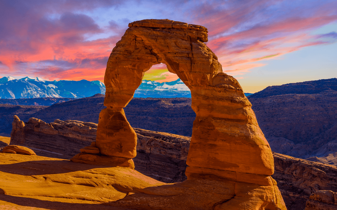 Delicate Arch at sunset with vibrant sky and mountain backdrop.